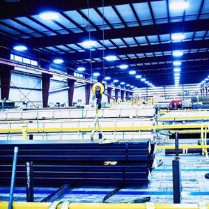 iso-img-29 Marmon Keystone A brightly lit industrial warehouse interior with stacked tube pipes and metals, yellow safety railings, and a hoist system hanging from the ceiling, showcasing a busy supplychain distributor environment.