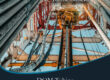 Marmon Keystone View looking up at steel pipes and equipment on an oil drilling rig, with text promoting Marmon/Keystone as your trusted metals distributor—with DOM tube and pipe in stock and ready to ship for oilfield supply chain needs.